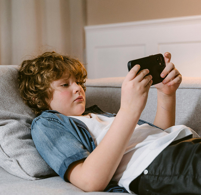 Child using a smartphone, reclining on a sofa in a casual setting. Child using a smartphone, reclining on a sofa in a casual setting.