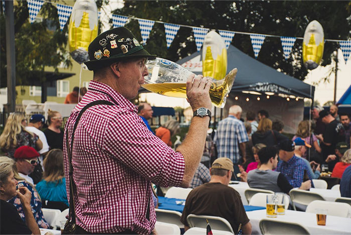 A man in a traditional Bavarian outfit drinking beer at a German festival, surrounded by people and festive decorations. A man in a traditional Bavarian outfit drinking beer at a German festival, surrounded by people and festive decorations.