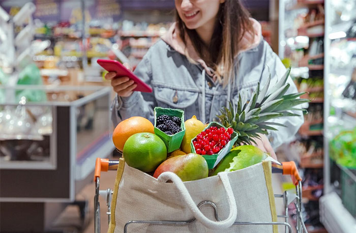 Woman in a grocery store with fruits in a cart, using a phone. Cultural insights from Germany influence her shopping habits. Woman in a grocery store with fruits in a cart, using a phone. Cultural insights from Germany influence her shopping habits.