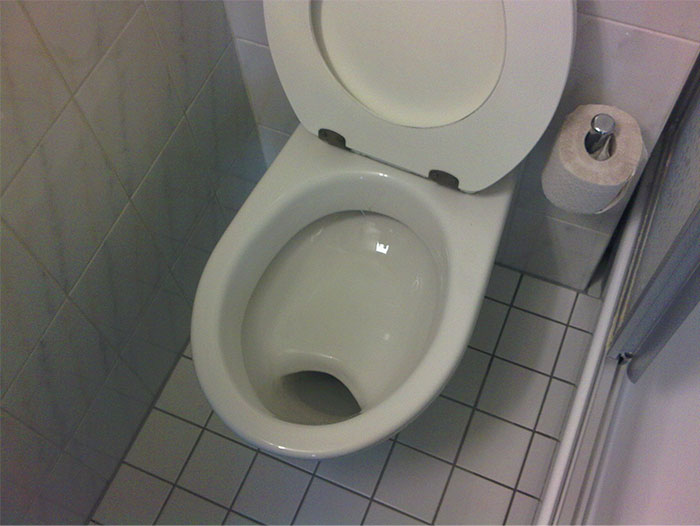 German cultural insight: a bathroom with a shelf toilet bowl and toilet paper on tiled floor. German cultural insight: a bathroom with a shelf toilet bowl and toilet paper on tiled floor.