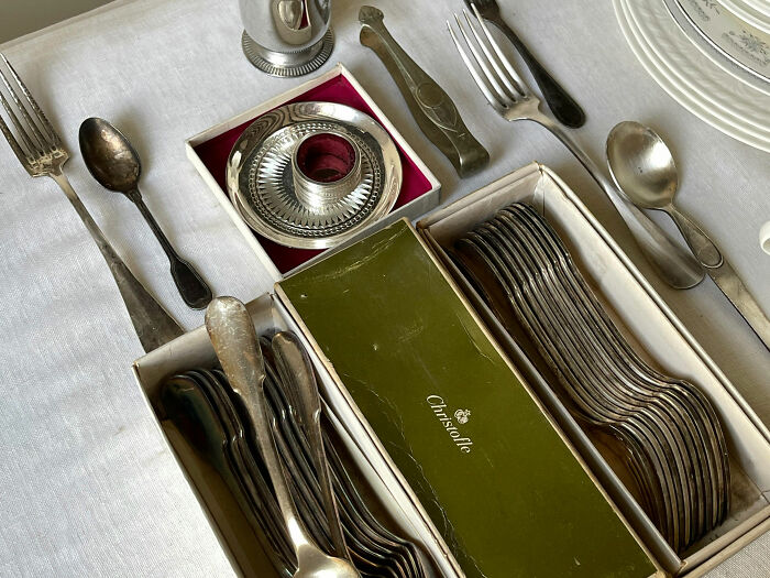 Silverware collection displayed on a white tablecloth, featuring boxed spoons, forks, and a Christofle brand box. Silverware collection displayed on a white tablecloth, featuring boxed spoons, forks, and a Christofle brand box.