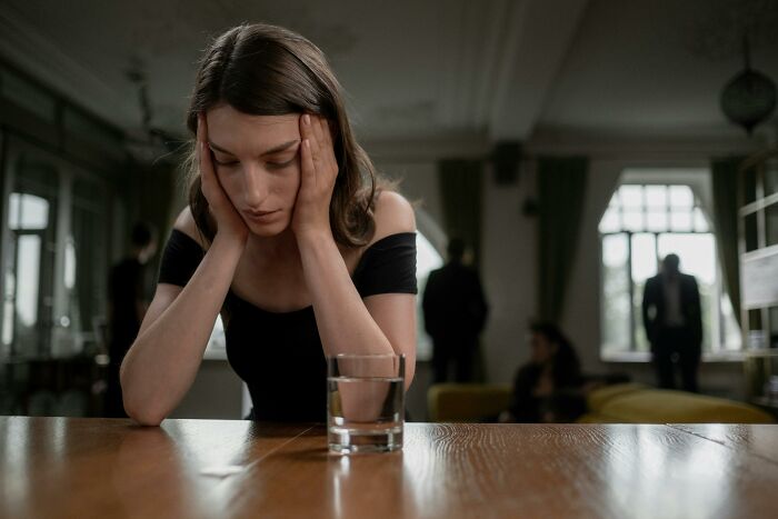 Woman in distress at a table with a glass of water, reflecting the silverware drama theme. Woman in distress at a table with a glass of water, reflecting the silverware drama theme.