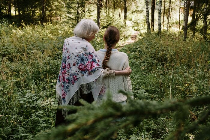 Elderly woman and child walking in a forest, wrapped in shawls, depicting family bonds and nature outing. Elderly woman and child walking in a forest, wrapped in shawls, depicting family bonds and nature outing.