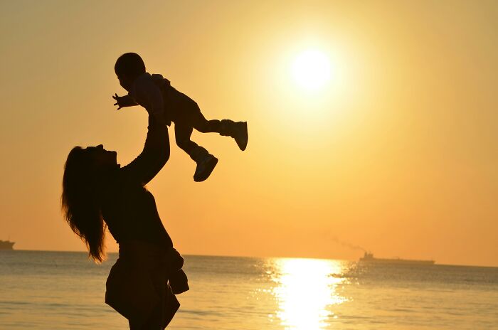 Silhouette of an adult lifting a child towards the golden sunset over the ocean. Silhouette of an adult lifting a child towards the golden sunset over the ocean.