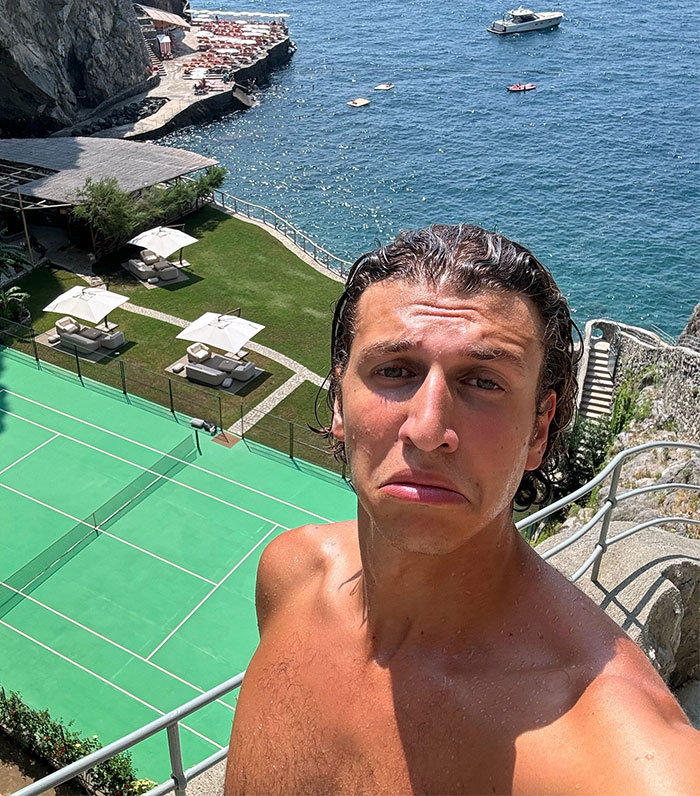 Man near cliffside tennis court with an ocean view, embodying a parody of luxury lifestyle online. Man near cliffside tennis court with an ocean view, embodying a parody of luxury lifestyle online.