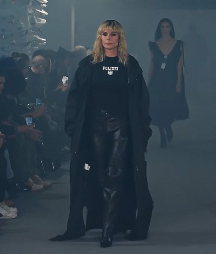 Model walks the runway in black leather attire at Paris Fashion Week amidst an audience capturing the moment. Model walks the runway in black leather attire at Paris Fashion Week amidst an audience capturing the moment.