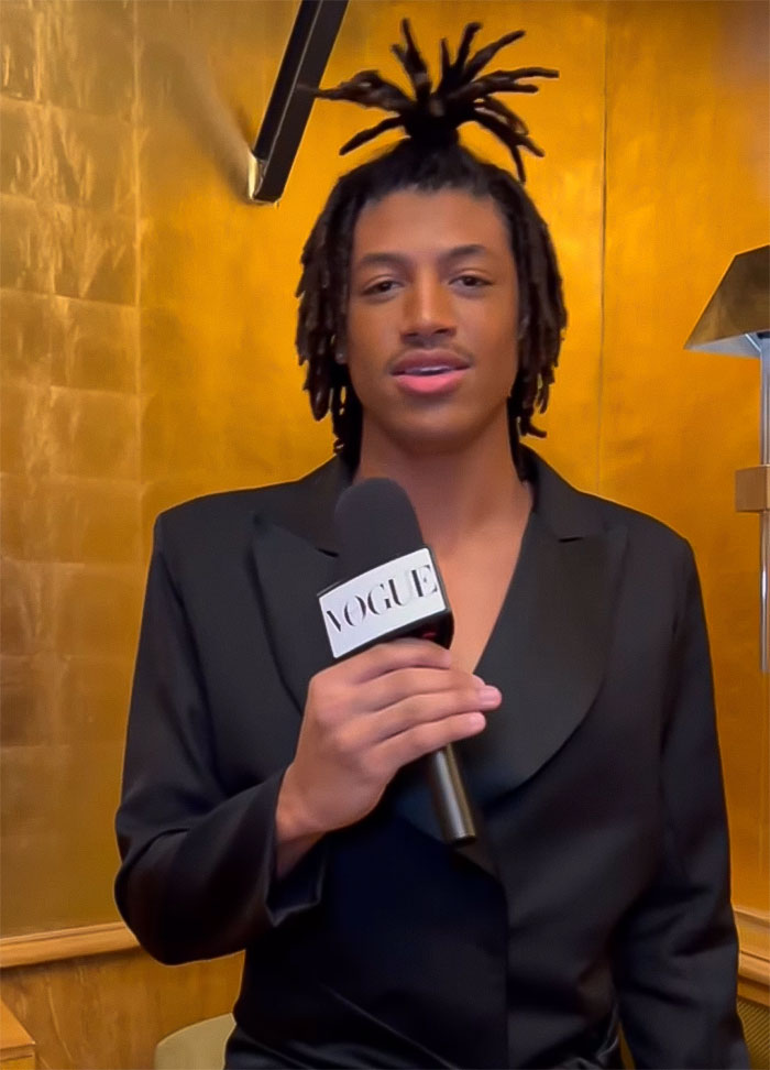 Young man holding Vogue microphone in black outfit at Paris Fashion Week runway event. Young man holding Vogue microphone in black outfit at Paris Fashion Week runway event.