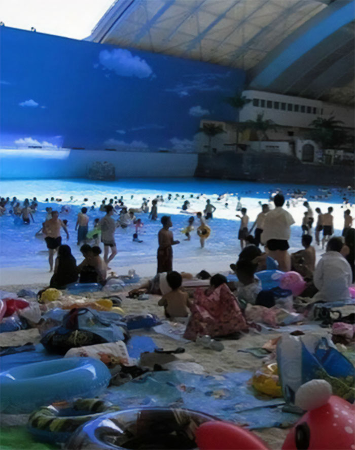 Indoor beach scene with people enjoying artificial waves, symbolizing humans of capitalism in leisure spaces.