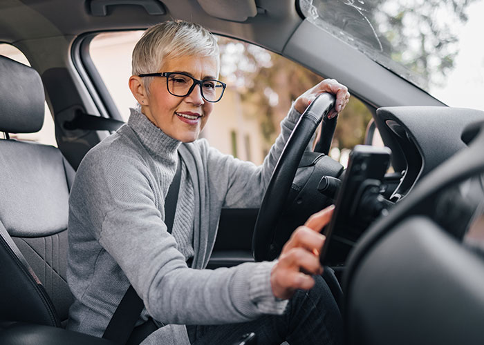Woman in a car wearing glasses and a gray sweater, interacting with the car's dashboard. Woman in a car wearing glasses and a gray sweater, interacting with the car's dashboard.