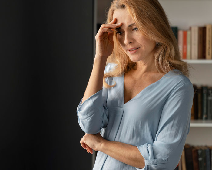 Woman in a thoughtful pose, wearing a blue blouse, standing in a room with bookshelves, pondering family responsibilities. Woman in a thoughtful pose, wearing a blue blouse, standing in a room with bookshelves, pondering family responsibilities.
