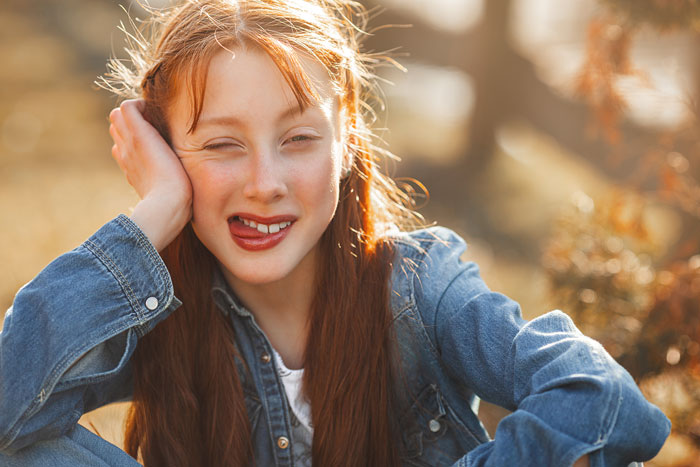 Girl in a denim jacket sitting outdoors, smiling playfully. Girl in a denim jacket sitting outdoors, smiling playfully.