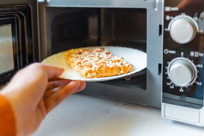 A person placing pizza in a microwave, possibly dealing with cooking drama. A person placing pizza in a microwave, possibly dealing with cooking drama.