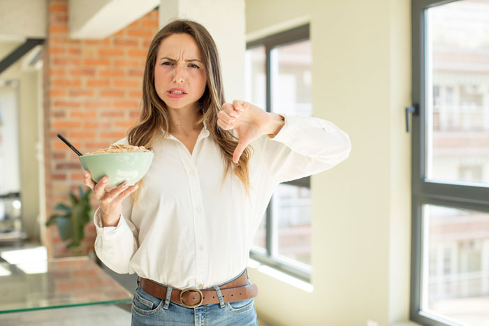 Woman expressing dissatisfaction in kitchen, holding bowl with thumb down, representing cooking drama. Woman expressing dissatisfaction in kitchen, holding bowl with thumb down, representing cooking drama.