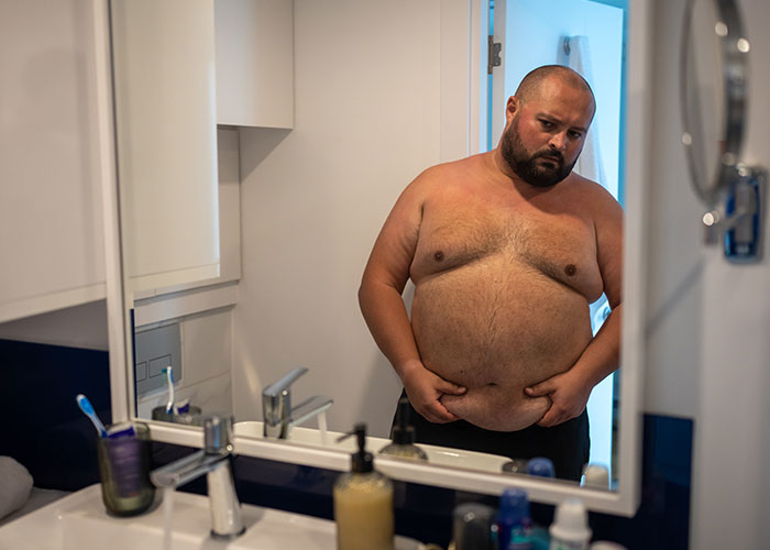 Overweight man looking at himself in the bathroom mirror, contemplating. Overweight man looking at himself in the bathroom mirror, contemplating.