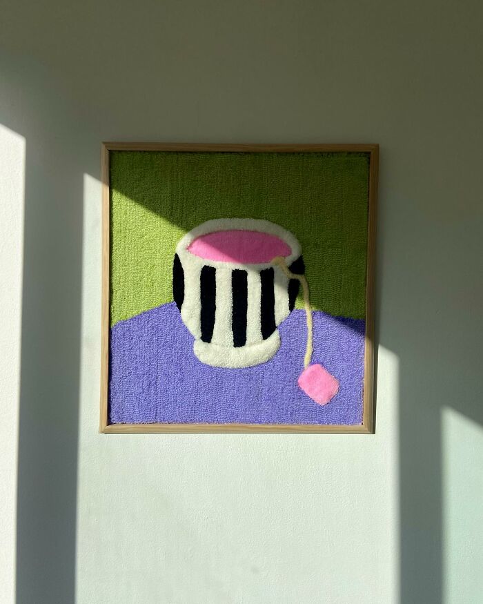 Framed tufted artwork by Cléa Delogu, featuring a stylized black and white cup on a green and purple background.