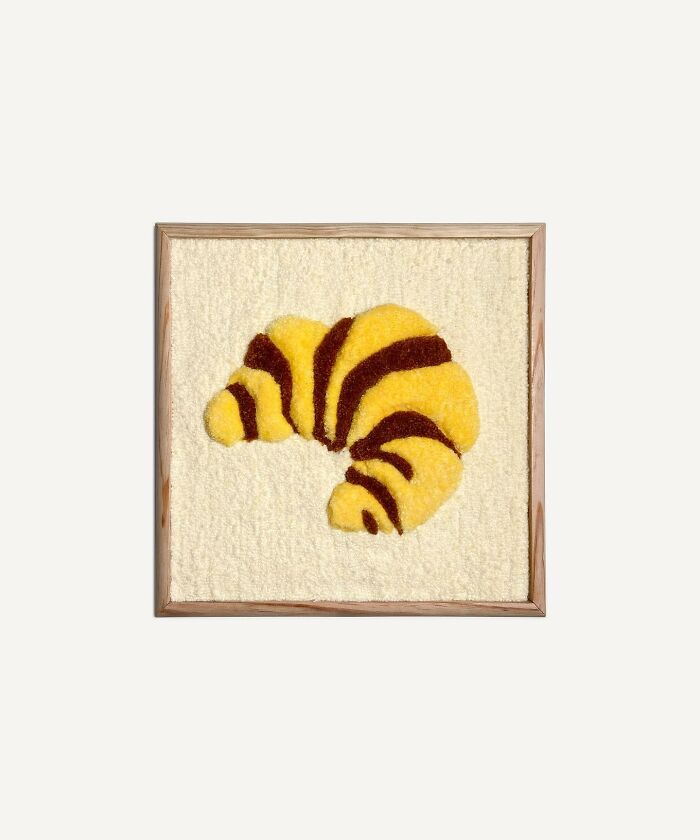 Tufted artwork featuring a croissant design by Cléa Delogu in a wooden frame.