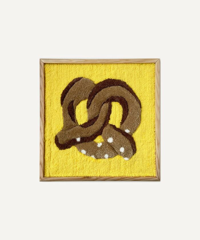Tufted artwork of a brown pretzel on a yellow background in a wooden frame.