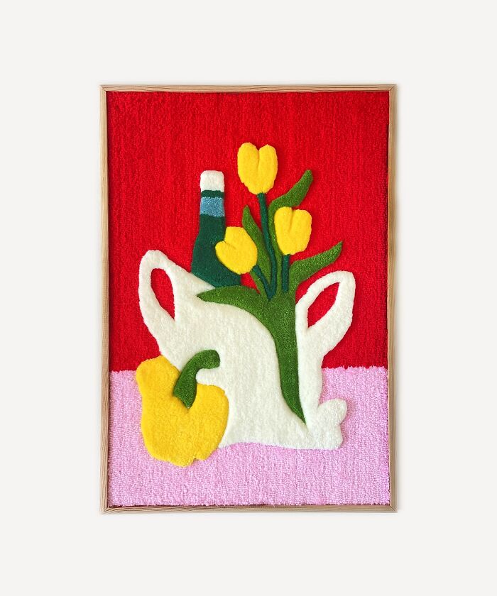 Tufted artwork featuring a vase with yellow tulips and a bottle on a vibrant red and pink background.