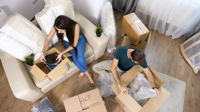 Couple unpacking boxes in a living room, surrounded by moving supplies and furniture. Couple unpacking boxes in a living room, surrounded by moving supplies and furniture.