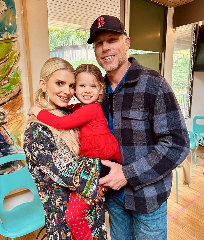 Family smiling together indoors, featuring Jessica Simpson and a man holding a young girl, both adults dressed casually. Family smiling together indoors, featuring Jessica Simpson and a man holding a young girl, both adults dressed casually.