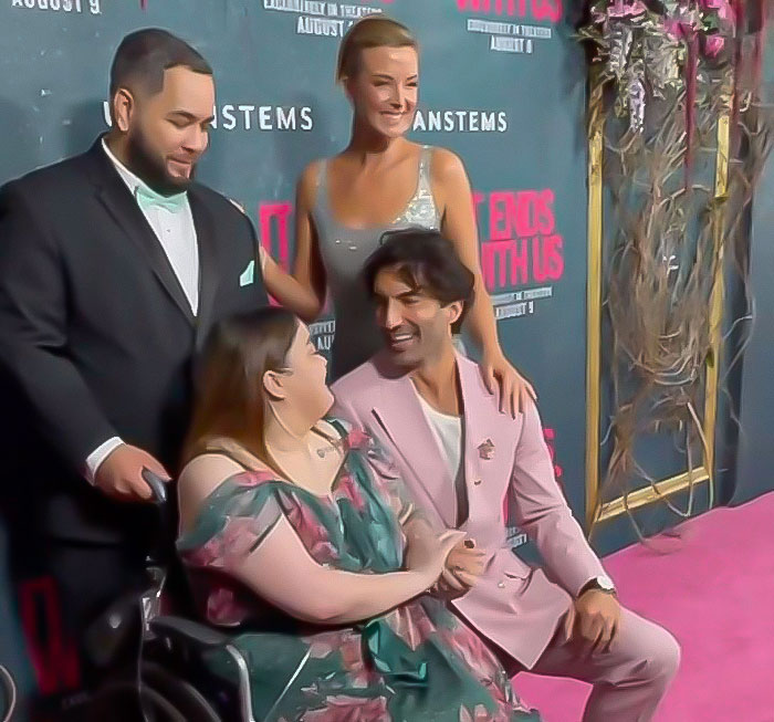 Group of people posing at a red carpet event, with a man in a pink suit smiling at a woman in a floral dress. Group of people posing at a red carpet event, with a man in a pink suit smiling at a woman in a floral dress.