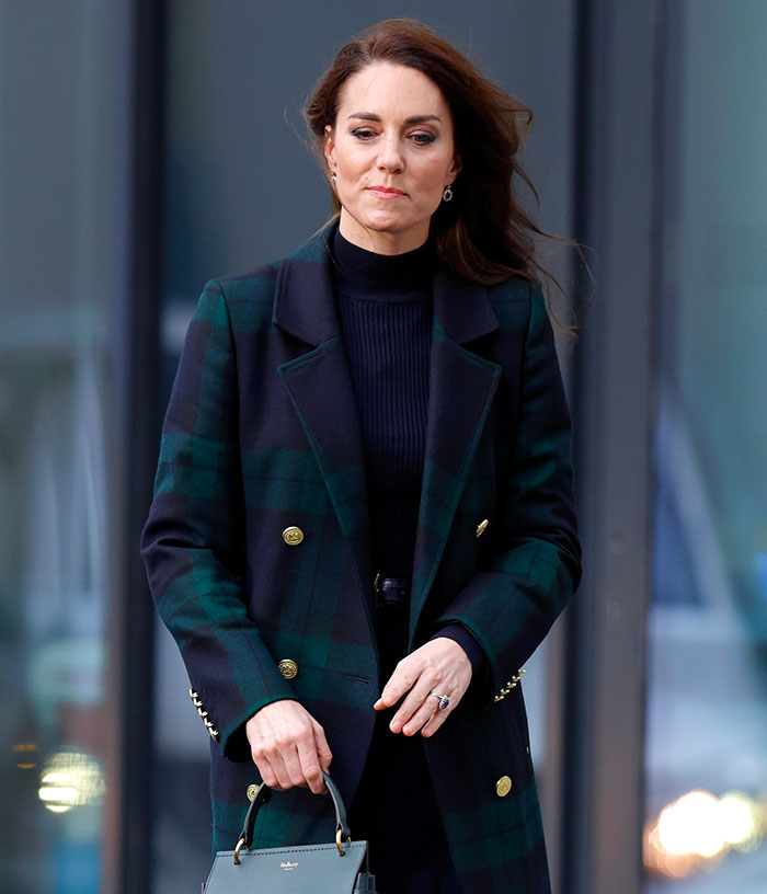 Woman wearing a ring and green coat, holding a handbag, sparking engagement ring mystery theories. Woman wearing a ring and green coat, holding a handbag, sparking engagement ring mystery theories.