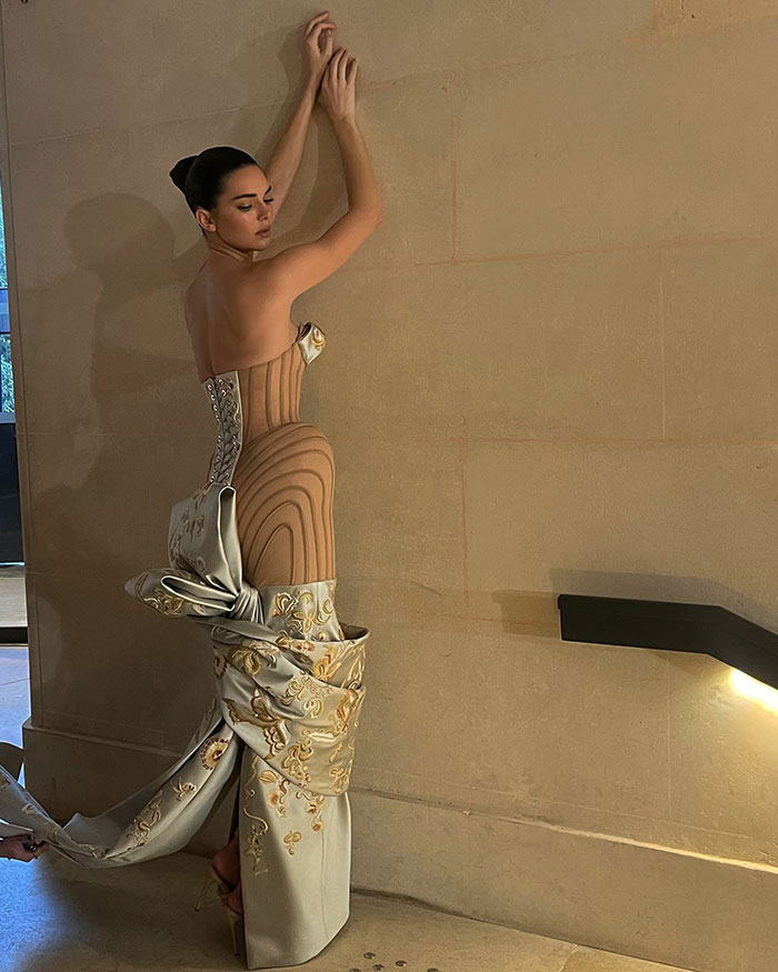 Kendall Jenner in a Paris Fashion Week dress with an intricate design, posing against a wall. Kendall Jenner in a Paris Fashion Week dress with an intricate design, posing against a wall.