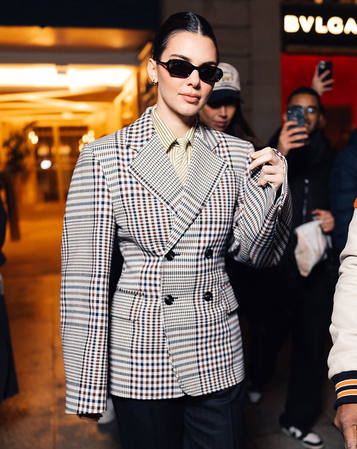 Kendall Jenner at Paris Fashion Week wearing a plaid suit and sunglasses, attracting attention from onlookers. Kendall Jenner at Paris Fashion Week wearing a plaid suit and sunglasses, attracting attention from onlookers.