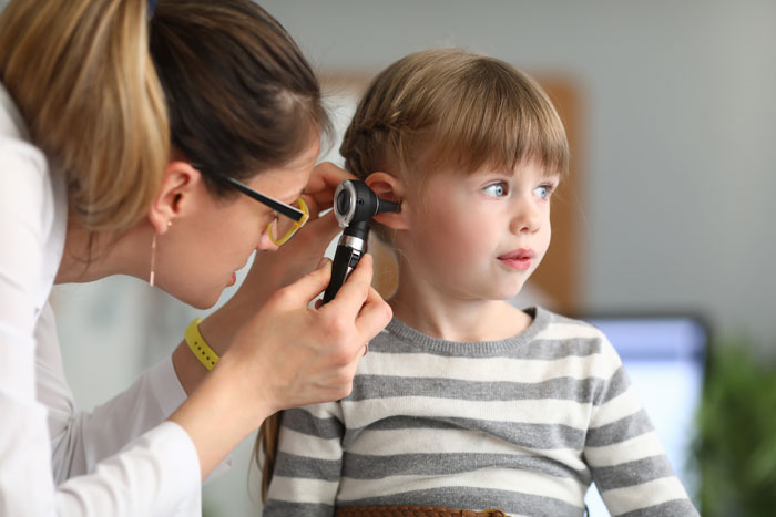Doctor examining young girl's ear with otoscope in a medical setting. Doctor examining young girl's ear with otoscope in a medical setting.