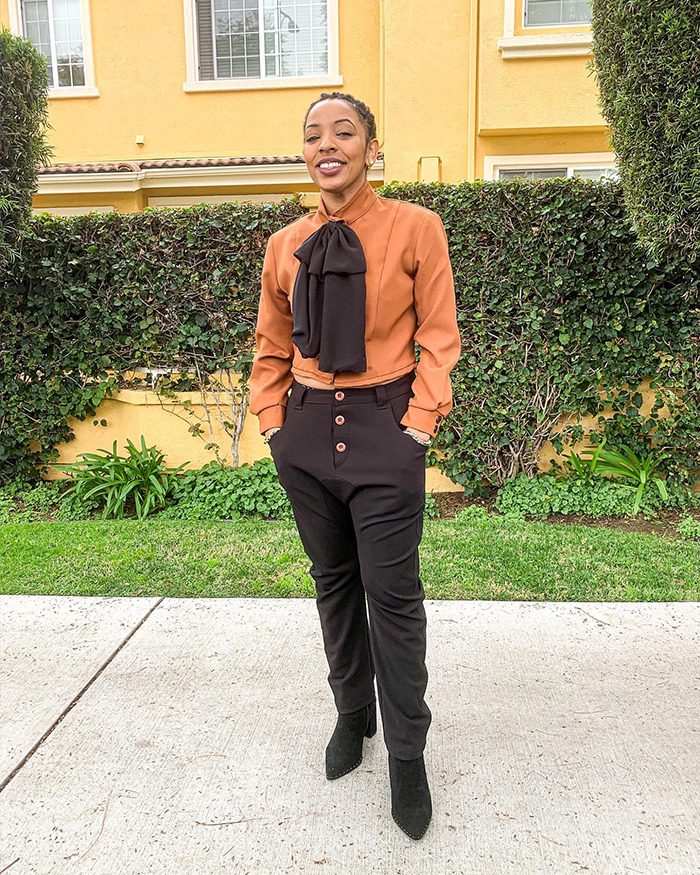 Black woman smiling outdoors in an orange blouse and black pants. Black woman smiling outdoors in an orange blouse and black pants.