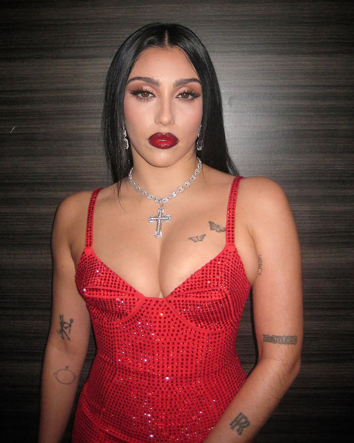 Lourdes Leon in a sparkling red bodysuit with tattoos, standing against a wooden backdrop. Lourdes Leon in a sparkling red bodysuit with tattoos, standing against a wooden backdrop.