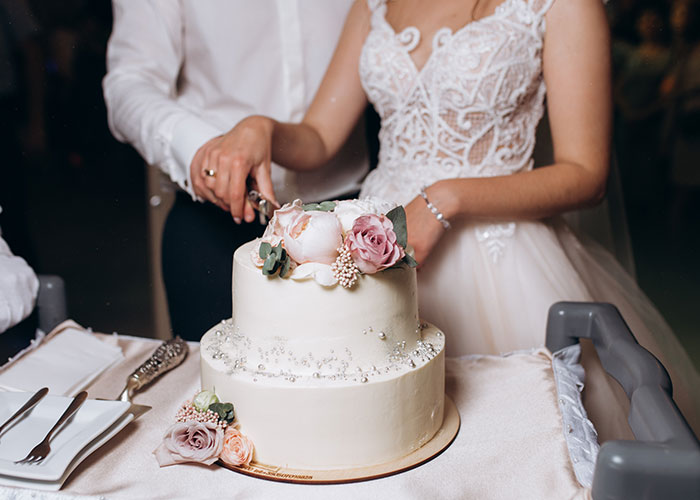 A bride and groom cutting a wedding cake, decorated with pink and white flowers on top. A bride and groom cutting a wedding cake, decorated with pink and white flowers on top.
