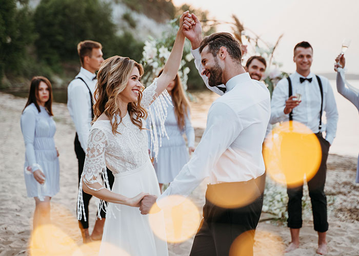 Bride dancing with groom on a beach with friends, smiling despite canceled wedding cake order. Bride dancing with groom on a beach with friends, smiling despite canceled wedding cake order.
