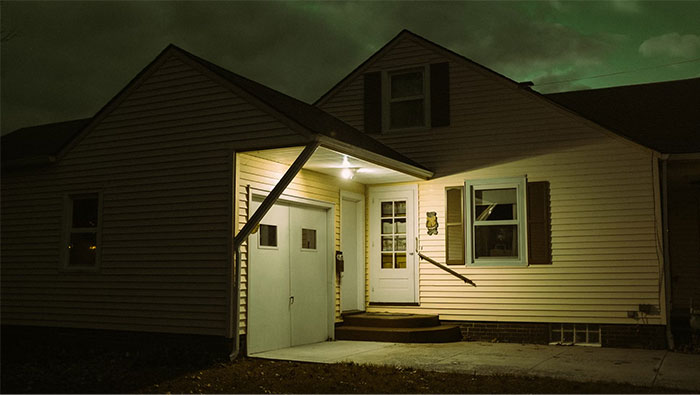 Night view of a dimly lit house exterior, front porch light on, suggesting a cautious home defense stance. Night view of a dimly lit house exterior, front porch light on, suggesting a cautious home defense stance.