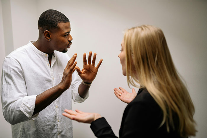 Man in a white shirt arguing with a woman in a black blazer, gesturing defensively in a heated discussion. Man in a white shirt arguing with a woman in a black blazer, gesturing defensively in a heated discussion.