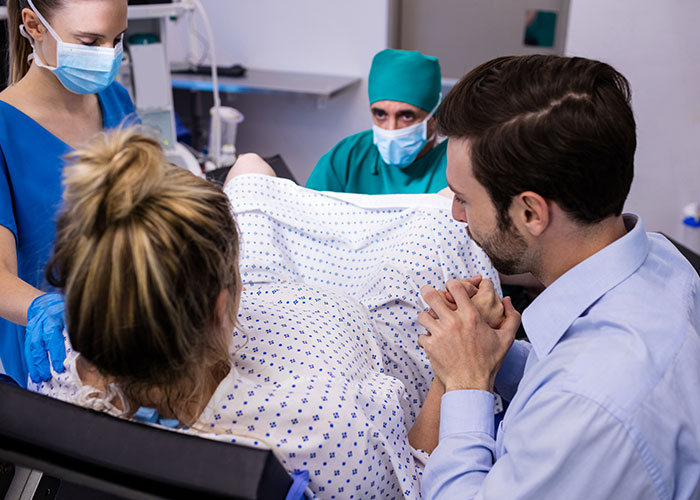 Man holds wife's hand in hospital during C-section, medical staff assisting childbirth. Man holds wife's hand in hospital during C-section, medical staff assisting childbirth.