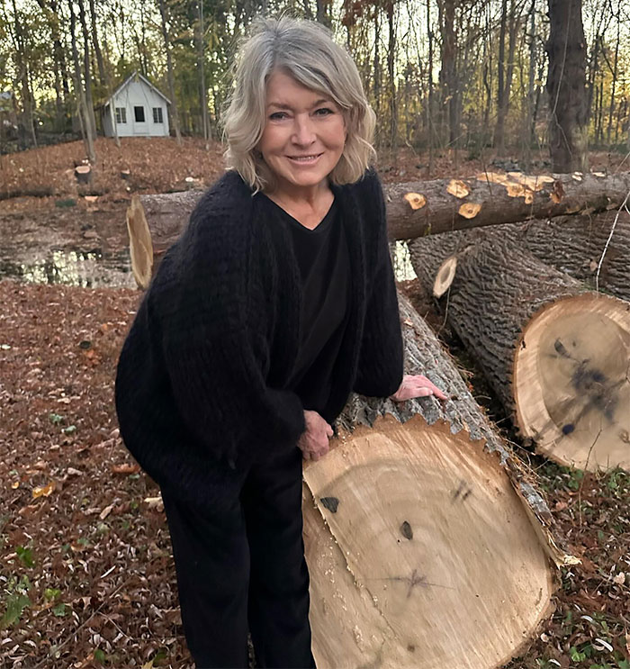 A woman in a black outfit smiles, leaning on a tree trunk in a wooded area, related to a cosmetics ad controversy. A woman in a black outfit smiles, leaning on a tree trunk in a wooded area, related to a cosmetics ad controversy.