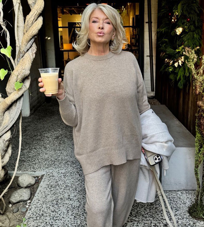 Woman in beige outfit poses confidently holding a drink, part of a Mac Cosmetics ad engaging fans. Woman in beige outfit poses confidently holding a drink, part of a Mac Cosmetics ad engaging fans.