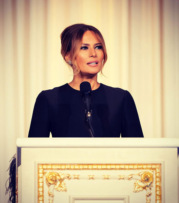 Melania Trump standing at a podium in a black dress, delivering a speech as First Lady. Melania Trump standing at a podium in a black dress, delivering a speech as First Lady.