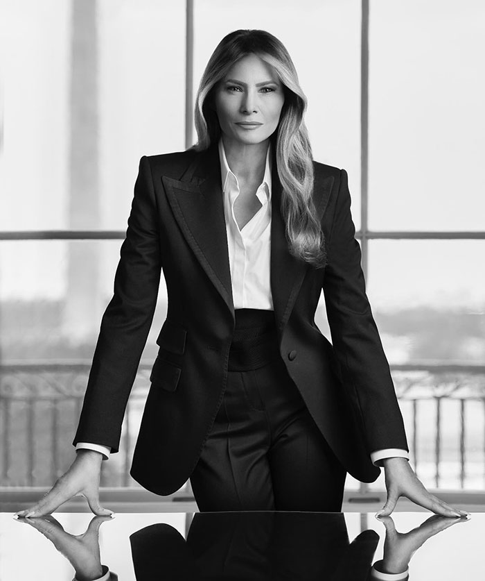 Melania Trump in a formal portrait, wearing a tailored black suit, standing confidently in a windowed room. Melania Trump in a formal portrait, wearing a tailored black suit, standing confidently in a windowed room.