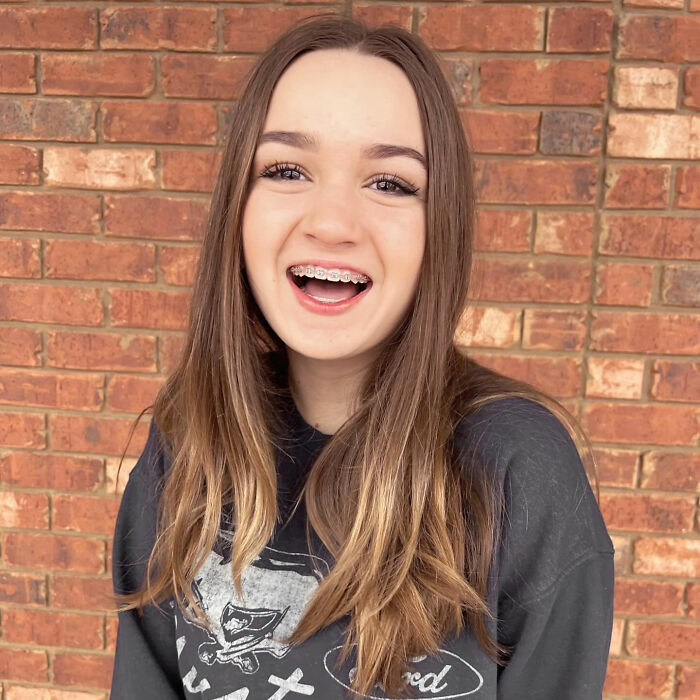 Teen girl smiling with braces, standing against a brick wall. Teen girl smiling with braces, standing against a brick wall.