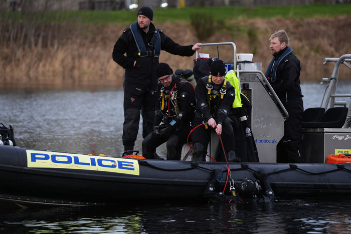 Police divers search a river for missing sisters, standing on a police boat. Police divers search a river for missing sisters, standing on a police boat.