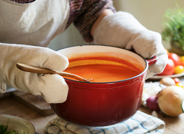 A red pot of spicy soup being stirred with love, held by a person wearing oven mitts. A red pot of spicy soup being stirred with love, held by a person wearing oven mitts.