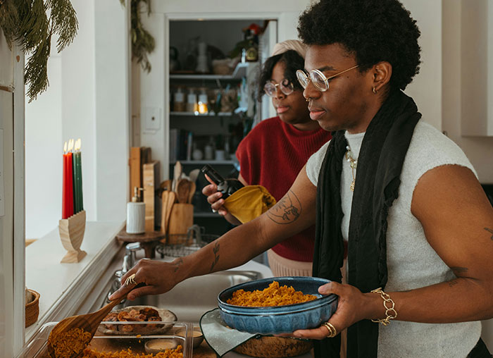 Person serving spicy food in a kitchen, with another person preparing ingredients. Person serving spicy food in a kitchen, with another person preparing ingredients.