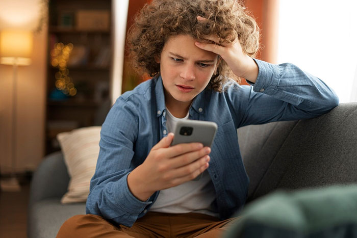 Young person on a couch, looking stressed while reading a message on a smartphone about toxic mom and inheritance. Young person on a couch, looking stressed while reading a message on a smartphone about toxic mom and inheritance.