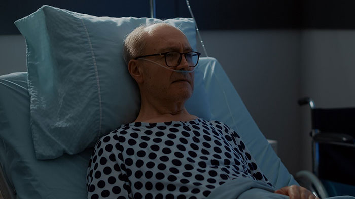 Elderly man in hospital gown, lying in a bed with medical equipment in the background. Elderly man in hospital gown, lying in a bed with medical equipment in the background.