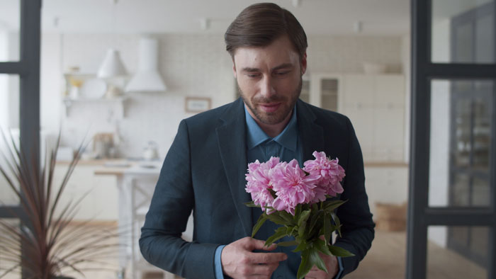 A man in a suit holding pink flowers in a modern kitchen, thinking about a family heirloom ring. A man in a suit holding pink flowers in a modern kitchen, thinking about a family heirloom ring.