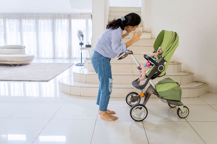 Woman facing a stroller in a modern living area, with sunlight streaming in through large windows. Woman facing a stroller in a modern living area, with sunlight streaming in through large windows.