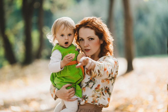 Woman holding child outdoors, pointing with a surprised expression. Woman holding child outdoors, pointing with a surprised expression.