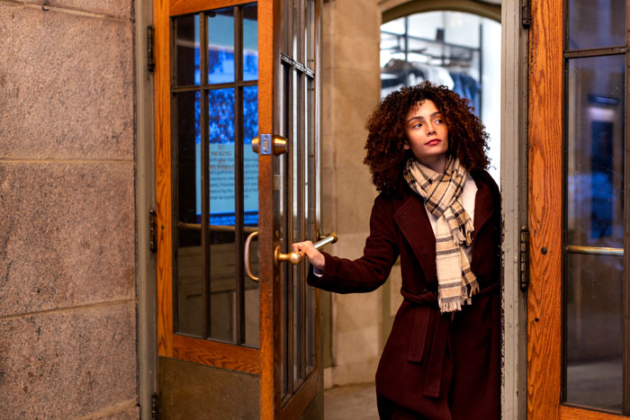 Woman opening a door in a building entrance, wearing a scarf and coat, appearing concerned about blocked access. Woman opening a door in a building entrance, wearing a scarf and coat, appearing concerned about blocked access.